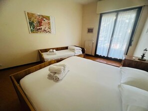 A hotel room with a large bed, a smaller bed, a radiator, and a window with curtains. - New Listing (Sanremo)