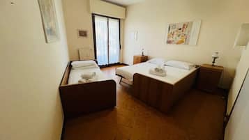 Ein Hotelzimmer mit zwei Betten, einem kleinen Tisch, einem Nachttisch, einem Heizkörper und einem Fenster mit Vorhängen.