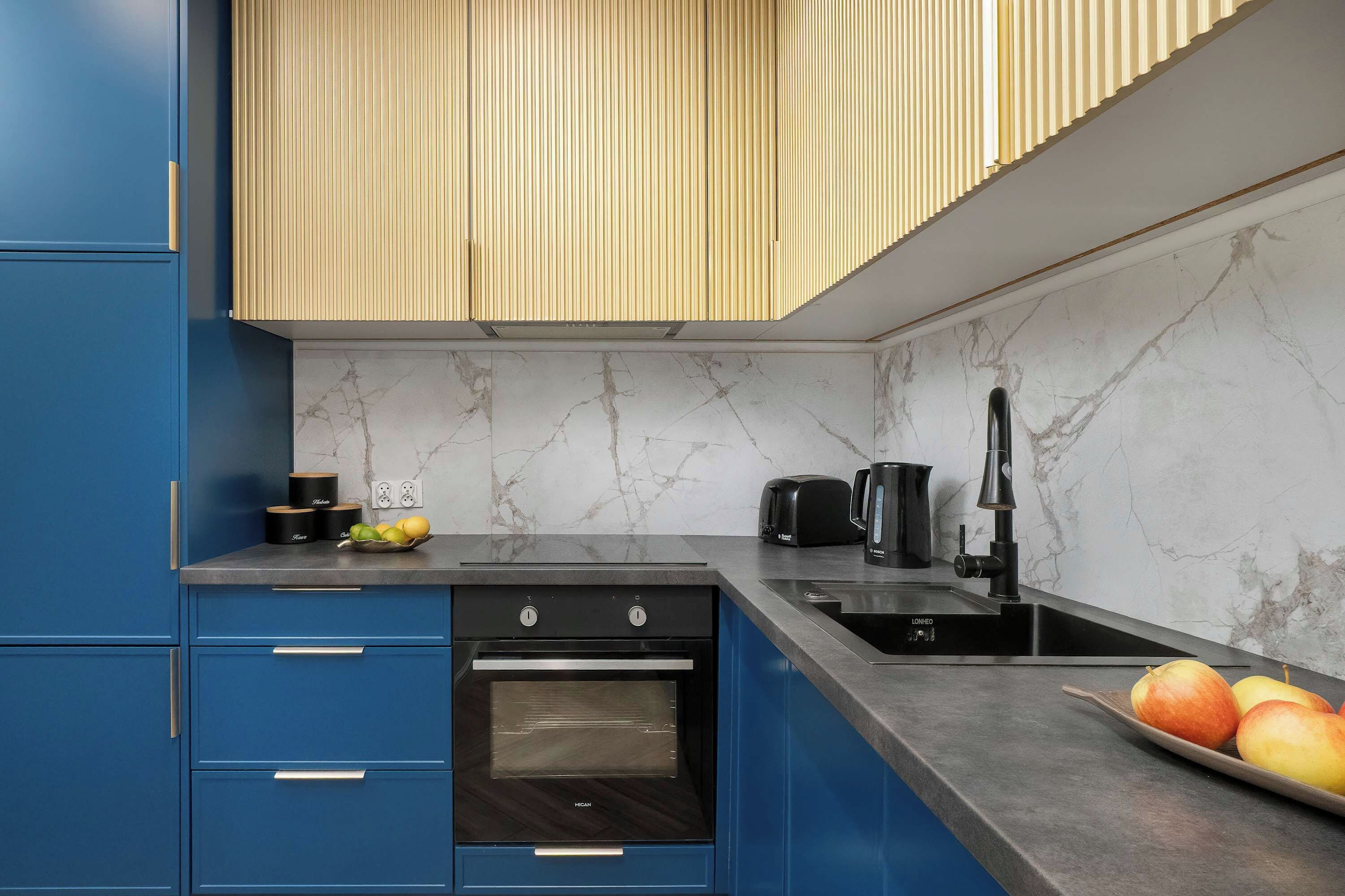Eine moderne Küche mit blauen Schränken, einem eingebauten Ofen, einer Spüle und einer Arbeitsplatte mit einer Obstschale.