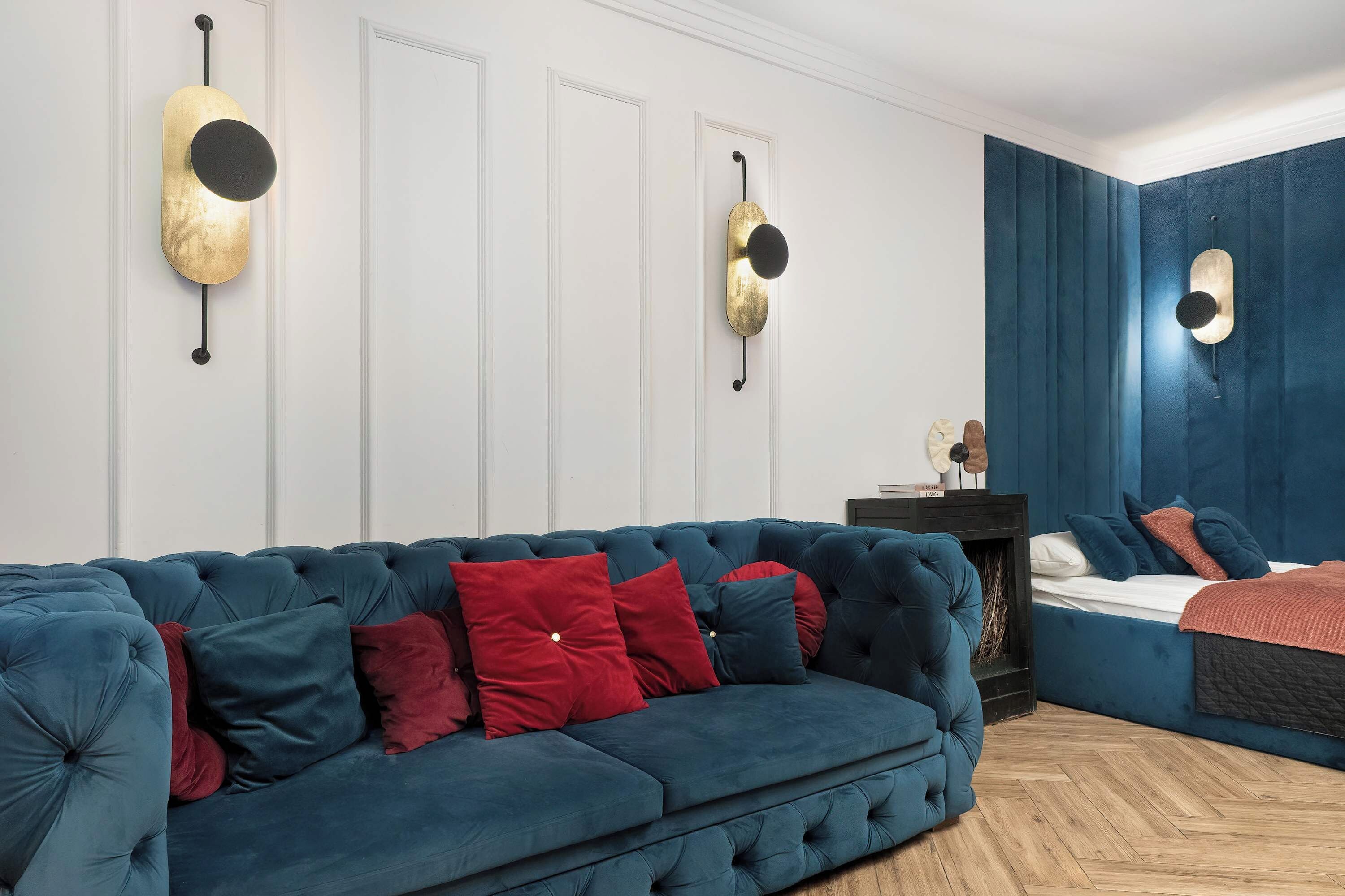 Une pièce avec un canapé bleu recouvert de tissu, un lit avec une tête de lit bleue et un luminaire fixé au mur.