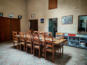 A dining area with a wooden table and chairs, a kitchen in the background, and a cabinet with dishes.