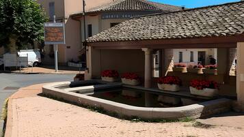 A building with a tiled roof, a paved courtyard with flower planters, and a sign with text.