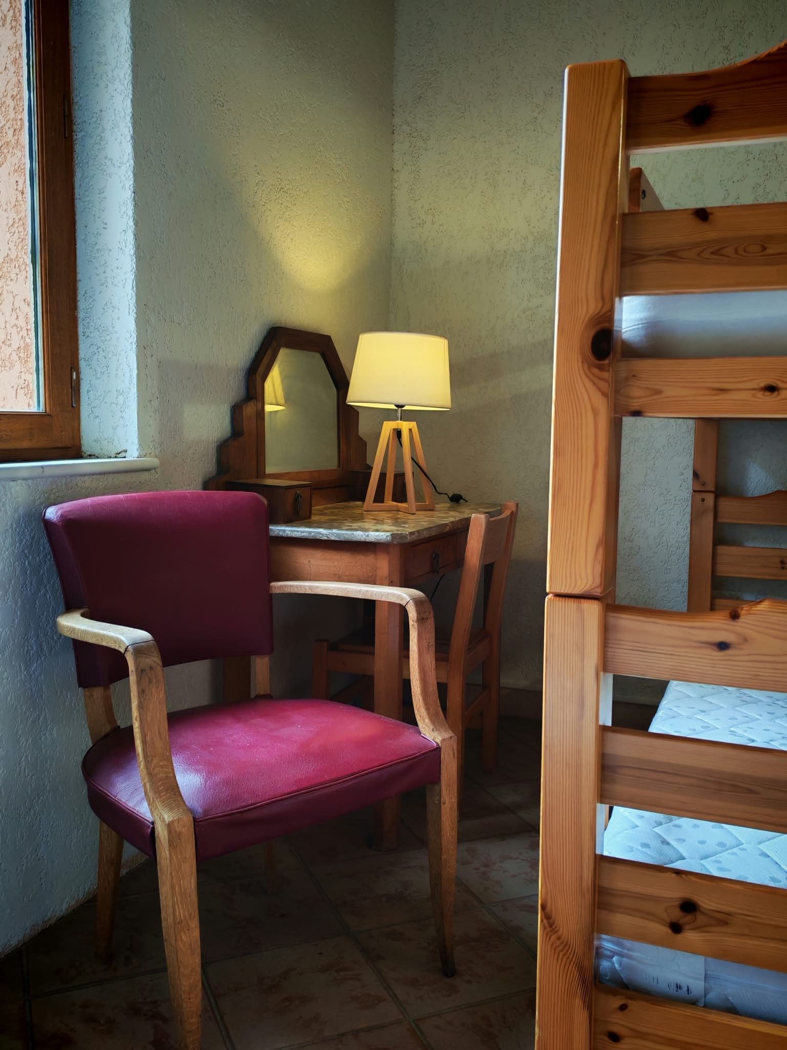 A bunk bed with a wooden headboard, a desk with a lamp, and a chair.