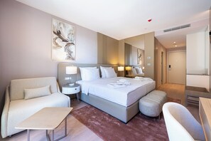 Una camera d'albergo con un letto grande, un divano, un tavolino e una panca. Sono presenti due comodini con lampade.