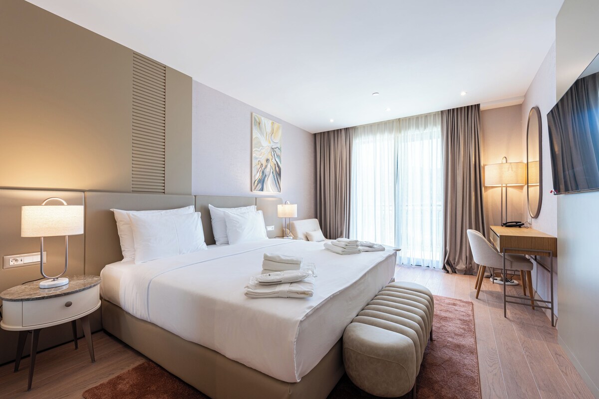 Una camera d'albergo moderna con un letto grande, lampade sui comodini, una scrivania e una sedia.
