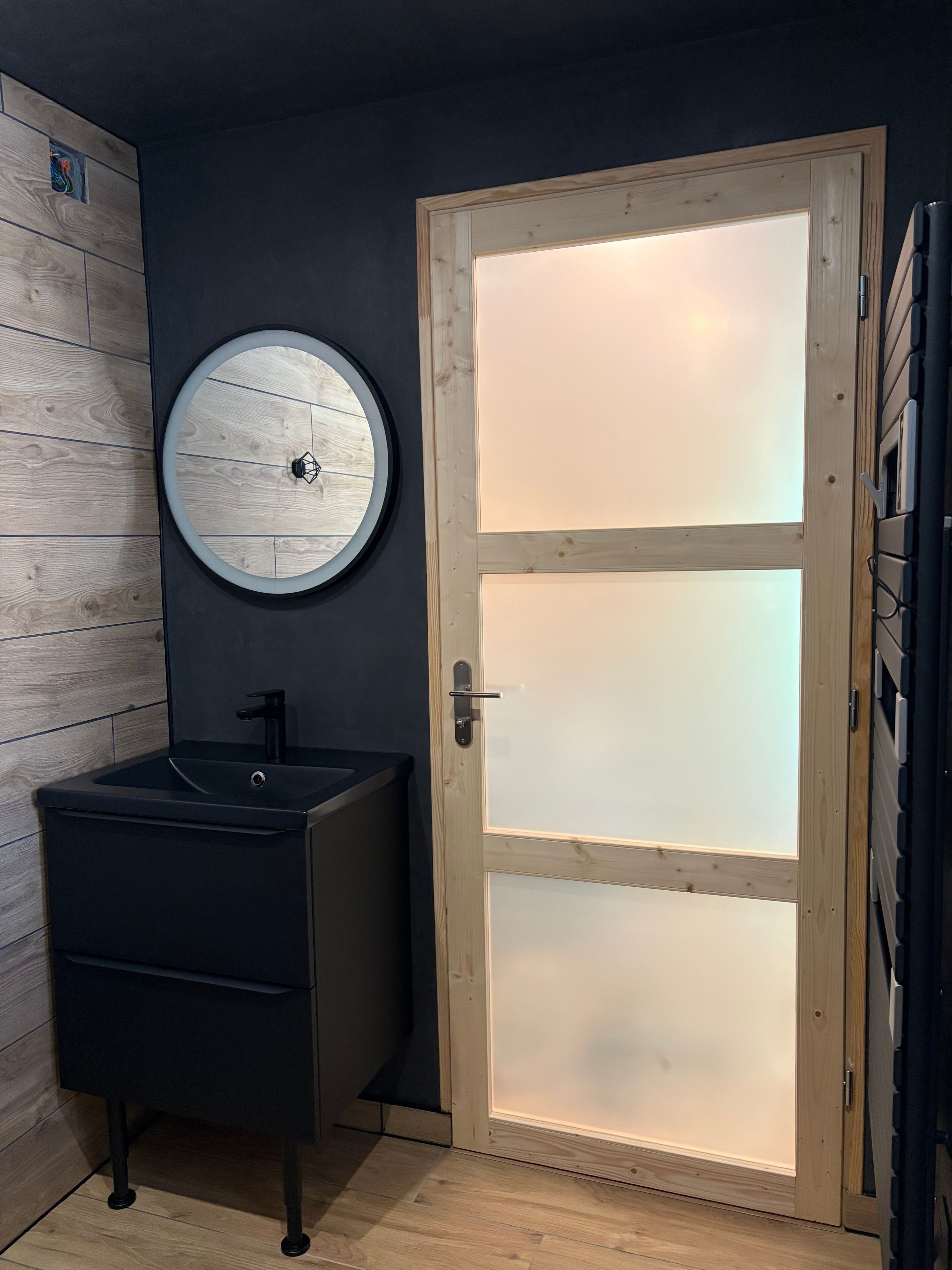 A bathroom with a black sink, a round mirror, and a frosted glass door.
