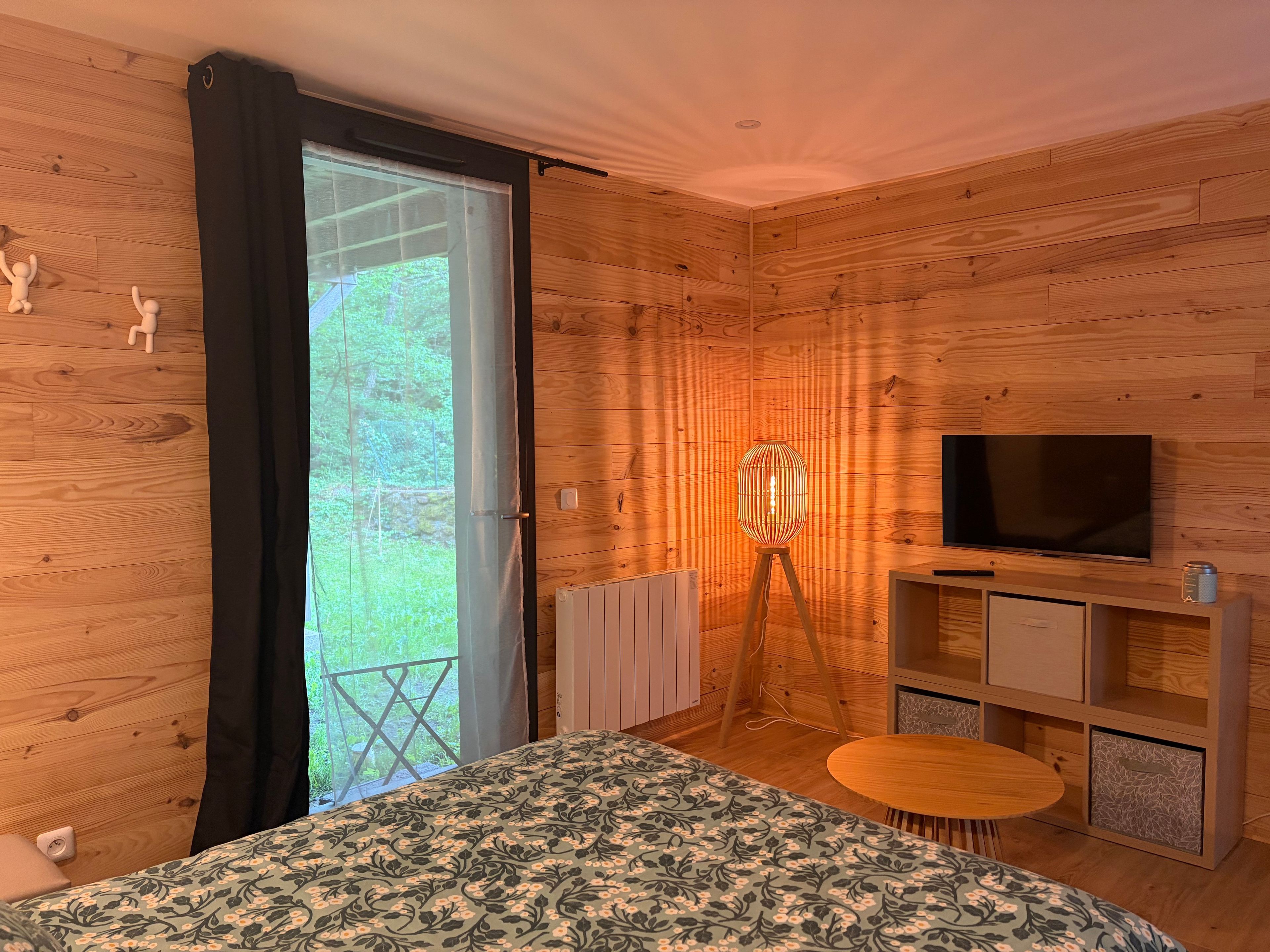 Une pièce aux murs lambrés, comprenant un lit, un téléviseur, une lampe sur pied et une petite table.