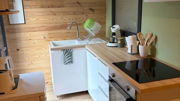 A compact kitchen with a wooden wall, a sink, a stove, and a countertop with utensils.