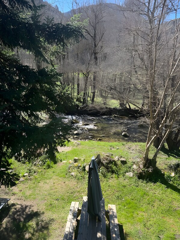 A wooden deck with a bench, overlooking a river with trees and a mountain in the background.