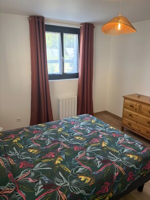 Ein Schlafzimmer mit einem Bett, einer Kommode, einem Fenster mit Vorhängen und einer Pendelleuchte.