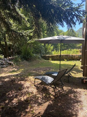 Eine Terrassenfläche mit Tisch und zwei Stühlen, umgeben von Bäumen und einer Steinmauer.