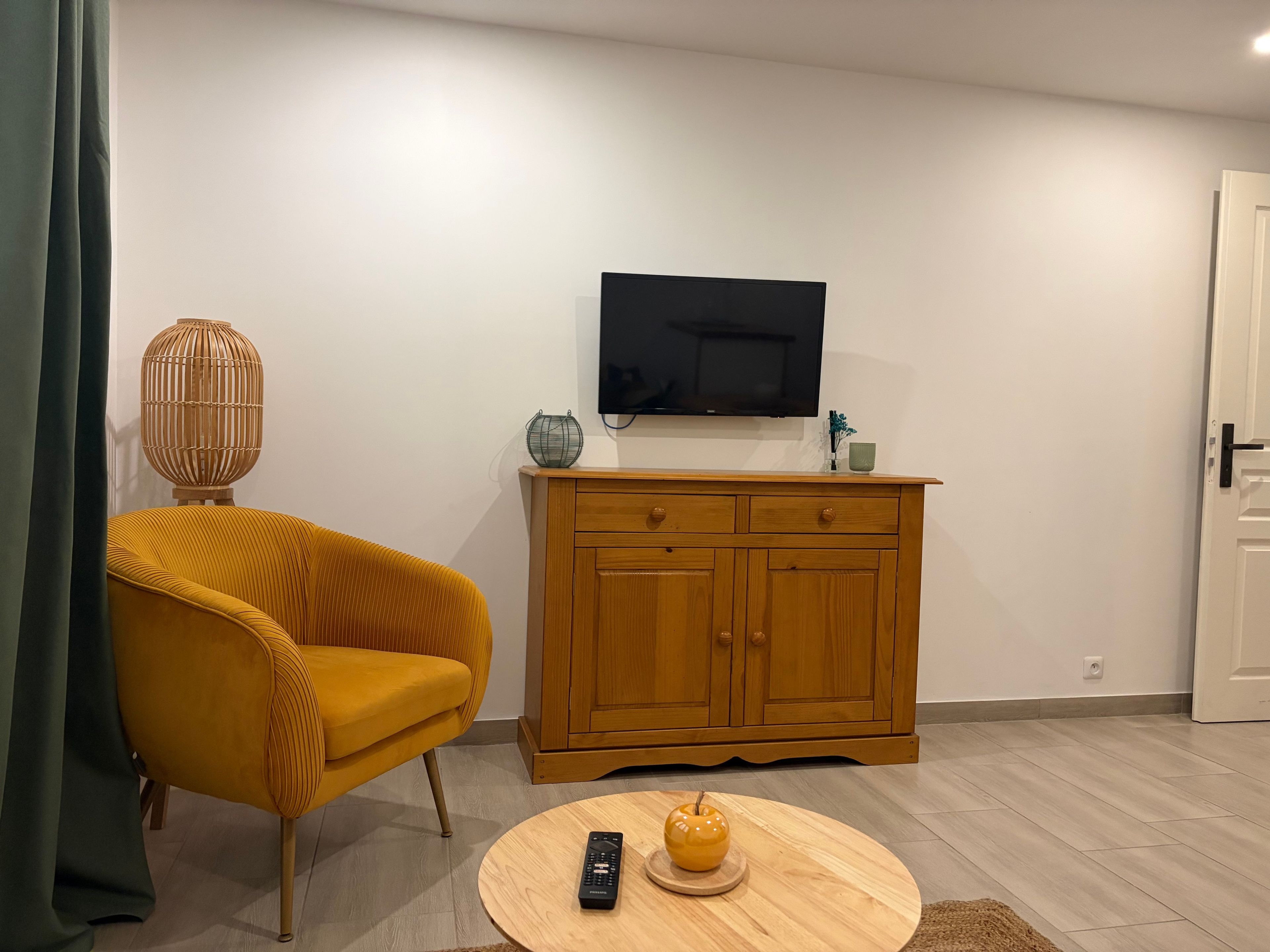 Un salon comprenant un canapé, un meuble en bois, un téléviseur et une table ronde sur laquelle se trouvent une télécommande et un objet décoratif.