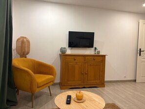 Ein Wohnzimmer mit einer Couch, einem Holzkasten, einem Fernseher und einem runden Tisch mit Fernbedienung und einer Dekoration.