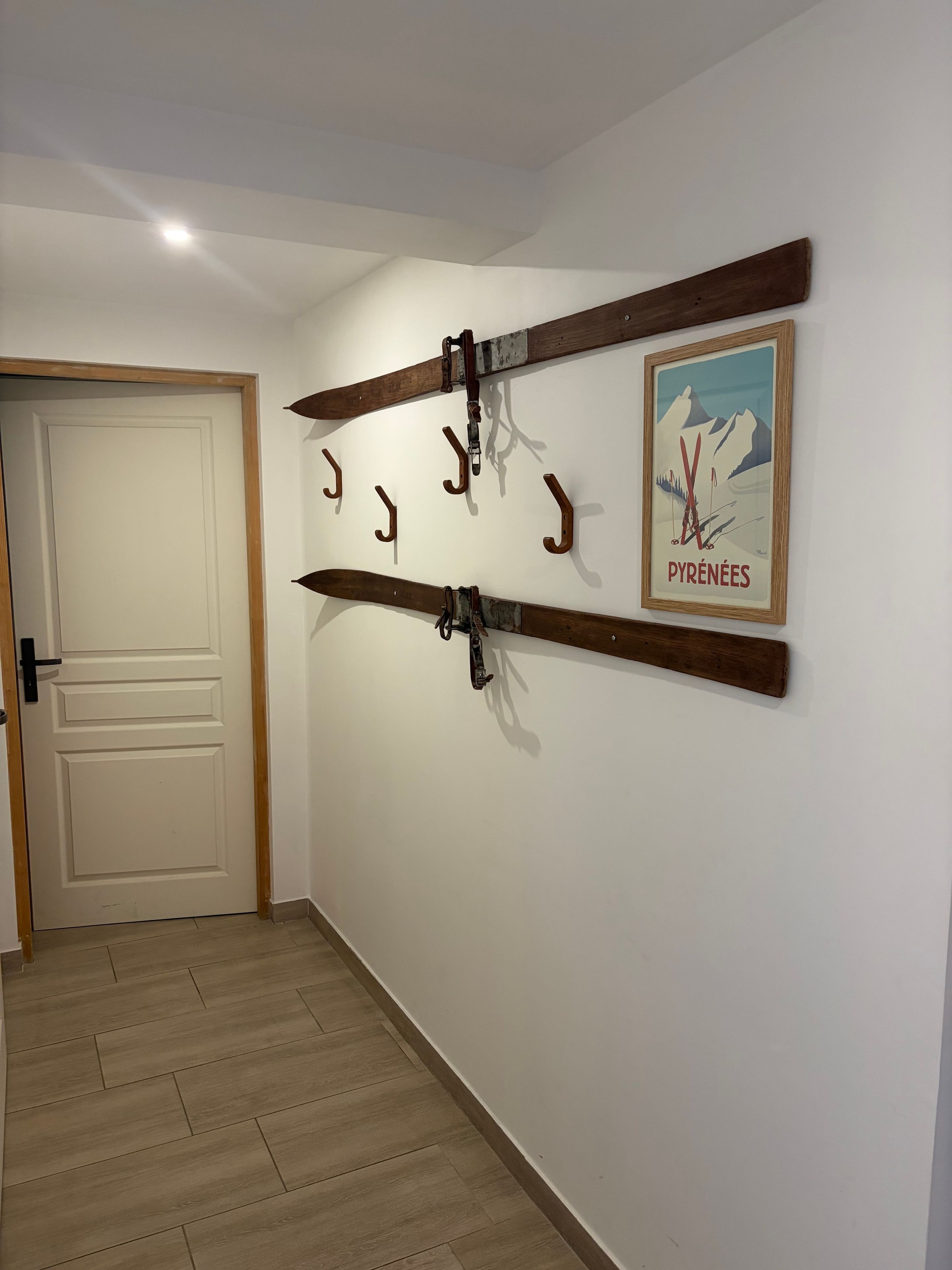 A hallway with a wooden door, a ski-themed wall art, and a wooden beam with hooks.