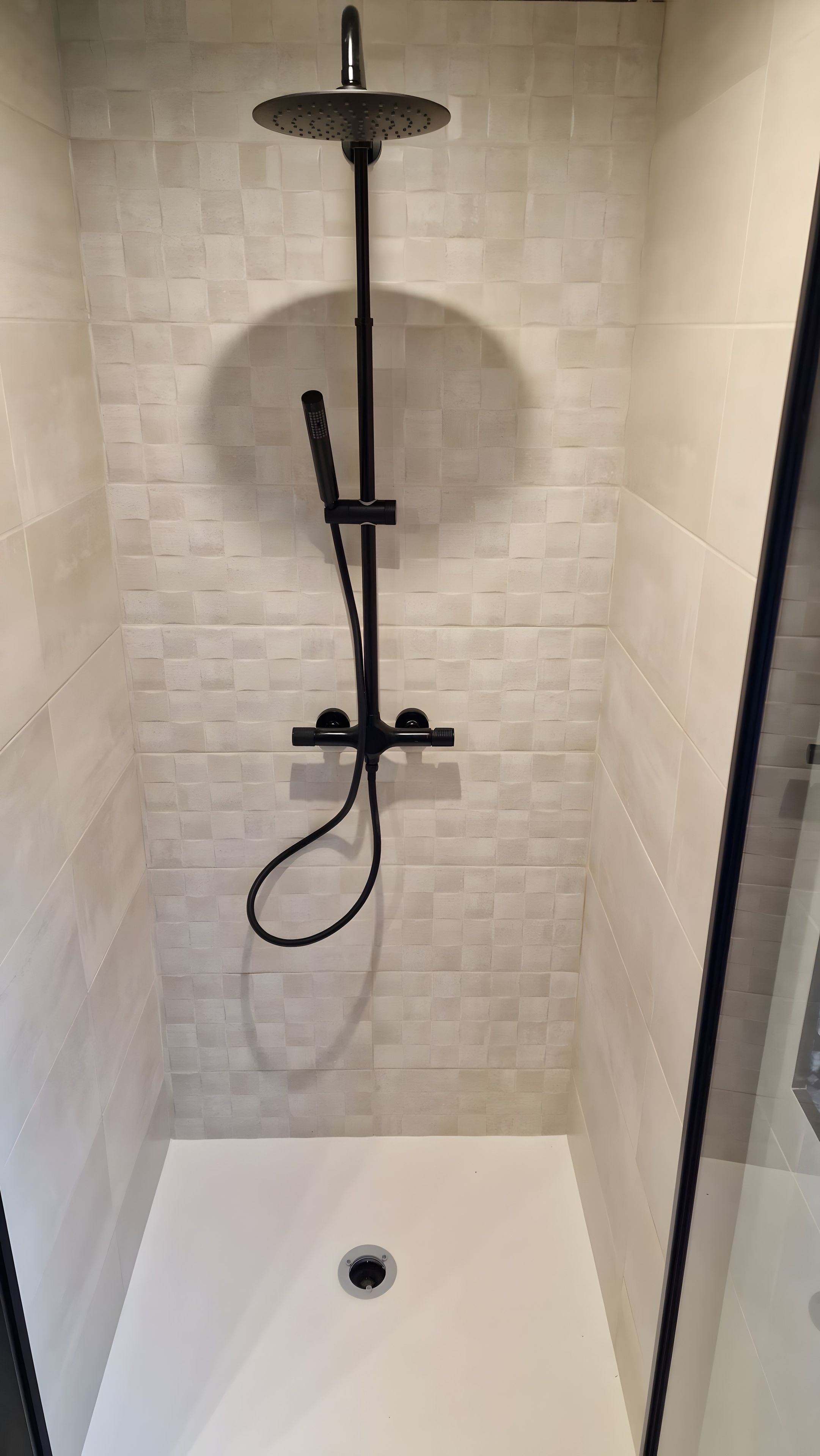 A shower with a handheld showerhead and a fixed overhead showerhead, a drain in the floor, and tiled walls.