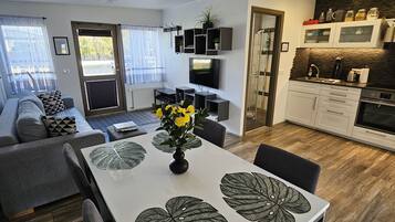 A modern kitchen with a built-in oven, a dining area with a table and chairs, and a living room with a sofa and a TV.