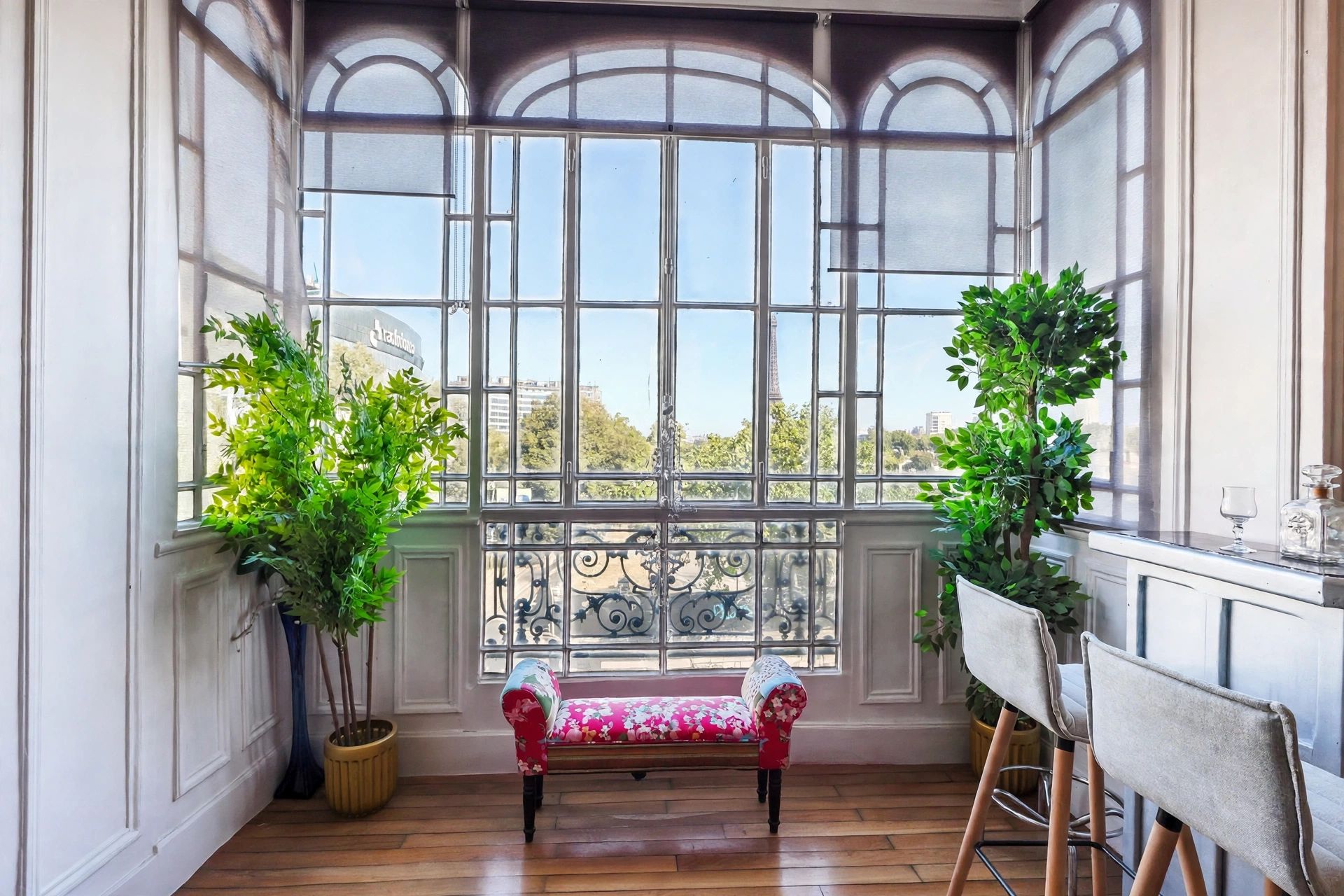 Habitación con un banco, dos plantas en macetas, una mesa con un vaso y vistas amplias a través de ventanas grandes.