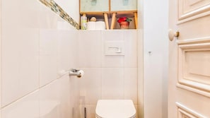 Un baño con inodoro, ducha y un estante con artículos de aseo.