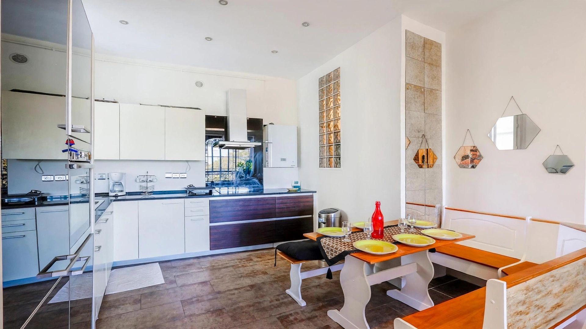 Cocina moderna con una isla central, comedor con banco y vistas al exterior.
