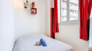Un dormitorio con cama, una ventana con cortinas y dos estantes en la pared con adornos.