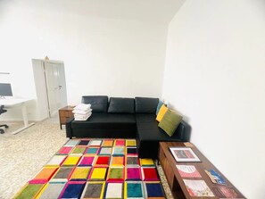Et værelse med en sort sofa, et farverigt tæppe, et lille bord med papirer og en hvid dør.