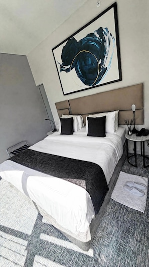 Una habitación de hotel moderna con una cama grande, cabecera, mesita de noche y una obra de arte colgada en la pared.