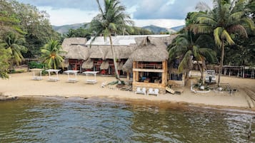 A beachfront property with thatched-roof buildings, white lounge chairs, and a view of the sea.