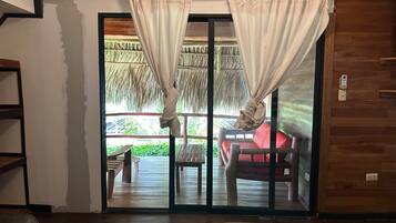 A room with a sliding glass door leading to an outdoor area with a red sofa and a thatched roof structure.
