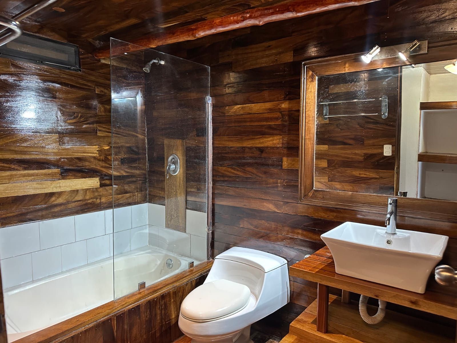 Une salle de bain avec un mur décoré en bois, une douche à parois de verre, des toilettes blanches et un lavabo blanc.