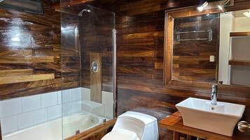 Une salle de bain avec un mur décoré en bois, une douche à parois de verre, des toilettes blanches et un lavabo blanc.