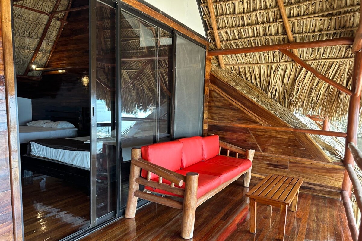 A room with a wooden floor, a red sofa, a wooden bench, and a thatched roof.