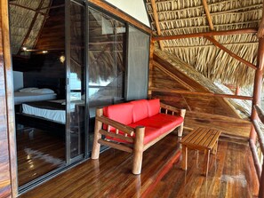 A room with a wooden floor, a red sofa, a wooden bench, and a thatched roof. - Hotel Bahía Guapinol (Mariscos)