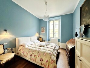 Et soveværelse med seng, stol, kommode, et vindue og en hængende lampe.