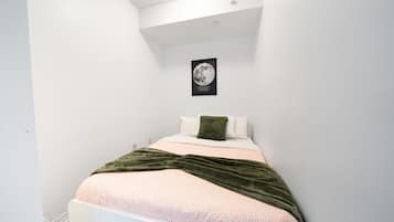 A bedroom with a bed, white walls, a ceiling light, and a framed picture on the wall.