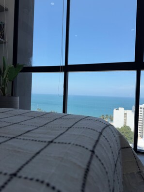 A room with a large window overlooking a body of water and buildings. - Luxury Apartment Suite – Ocean View, Steps from the Beach. (Gaira)