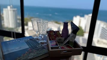 Une table avec un livre, des lunettes, des en-cas et une bouteille, avec vue sur la mer et les bâtiments.