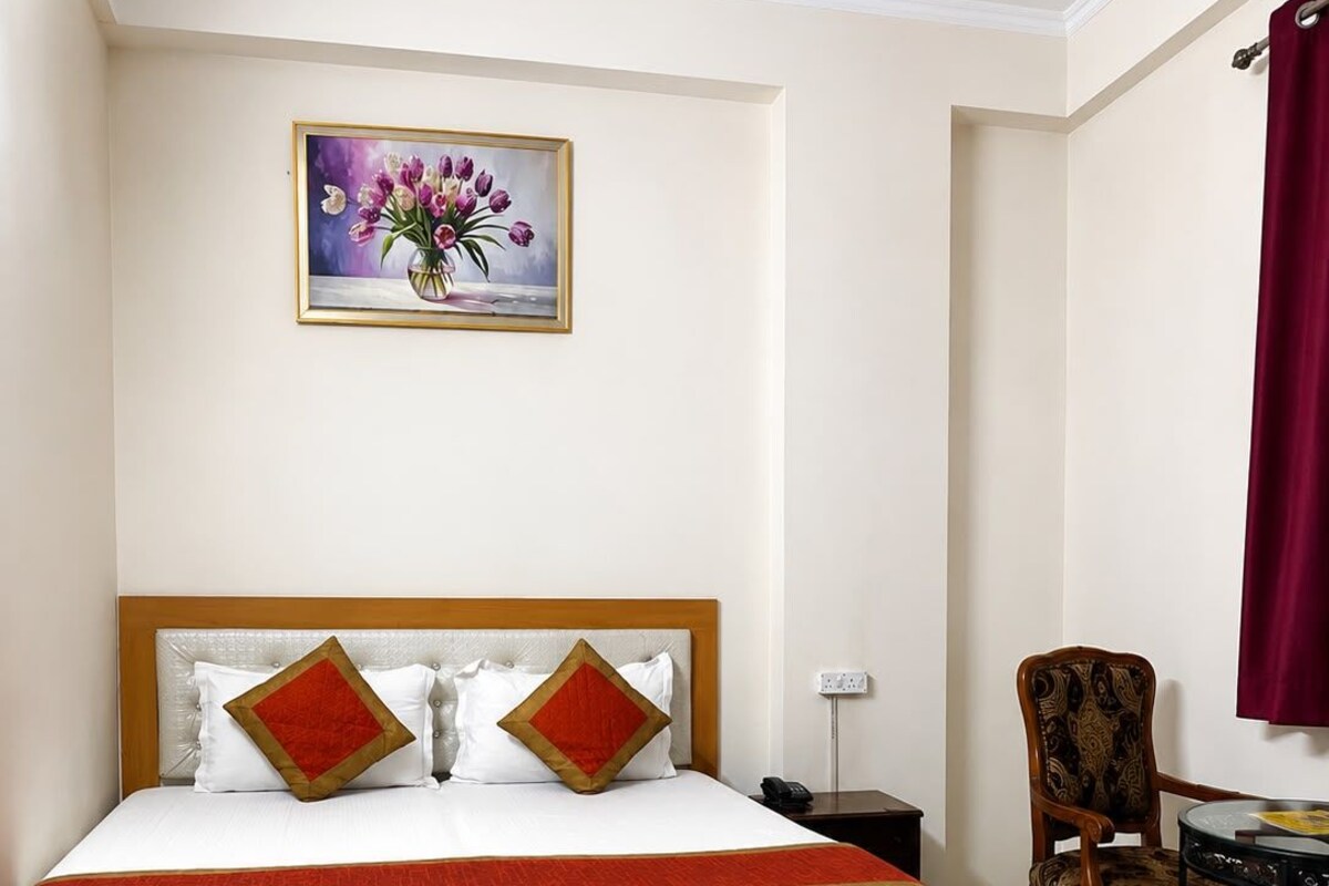 A hotel room with a large bed, a bedside table, a chair, a desk, and a painting on the wall.