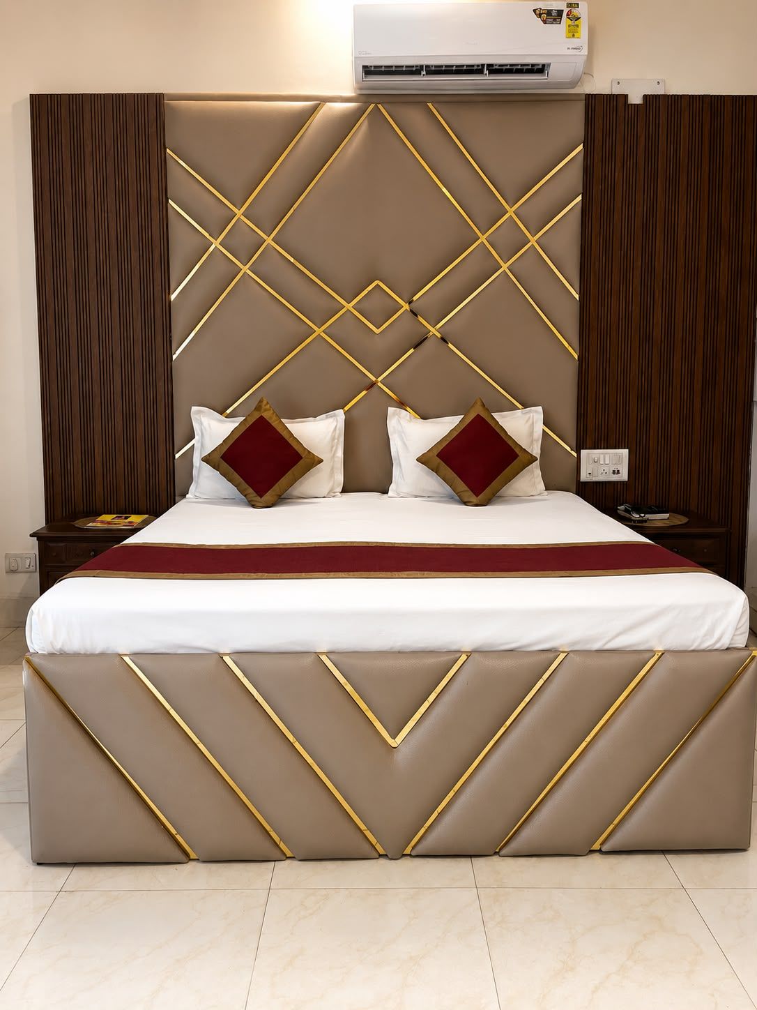 Een hotelkamer met een groot bed, een hoofdeinde met geometrische patronen en een airconditioning boven het bed.