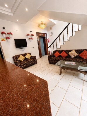 A living room with a sofa set, a coffee table, a flat-screen TV, and a staircase. - Hotel Swisston Palace (New Delhi)