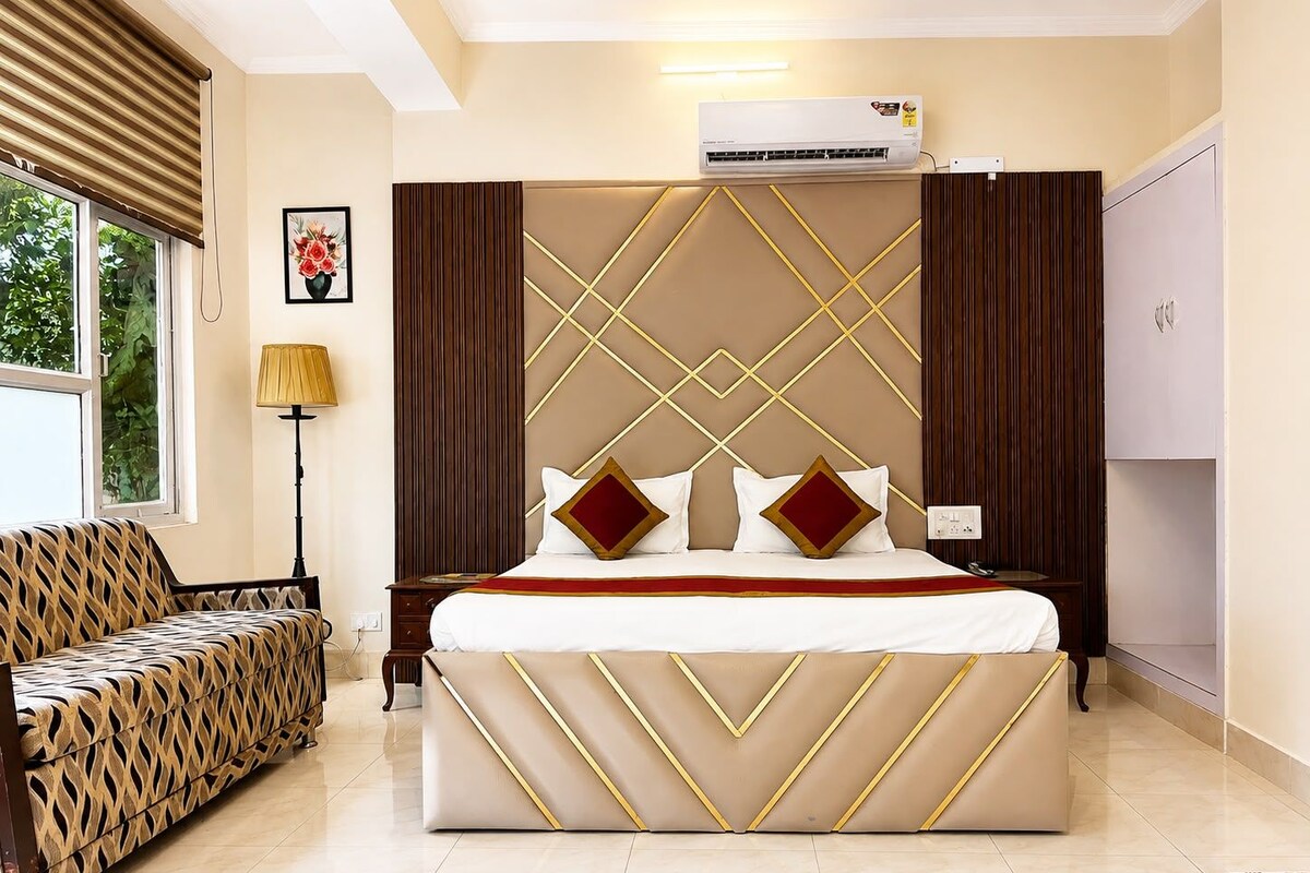 A hotel room with a large bed, a sofa, a lamp, and an air conditioning unit.