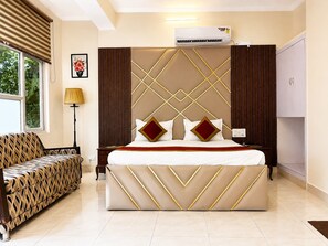A hotel room with a large bed, a sofa, a lamp, and an air conditioning unit. - Hotel Swisston Palace (New Delhi)