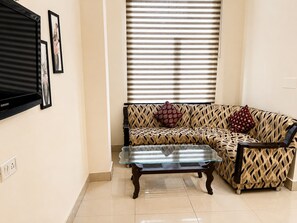 A living room with a sofa, a glass coffee table, and a flat-screen TV mounted on the wall. - Hotel Swisston Palace (New Delhi)