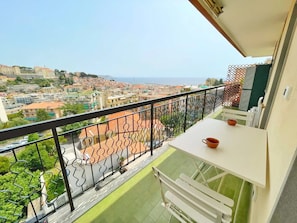En balkon med udsigt over en kystby, et hvidt bord og en rød kop.