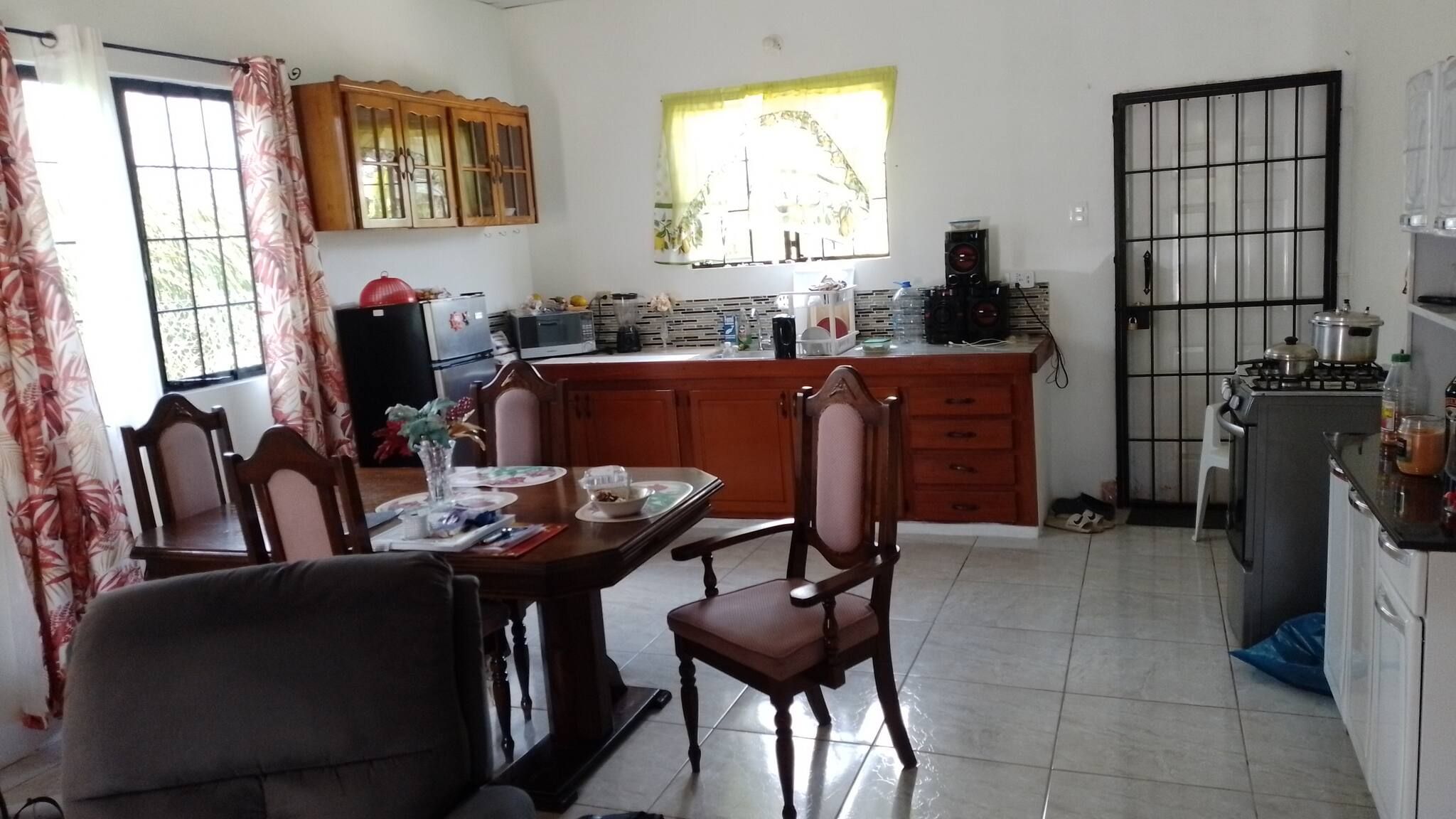 A kitchen with a dining table, chairs, a refrigerator, a stove, and a window with curtains.