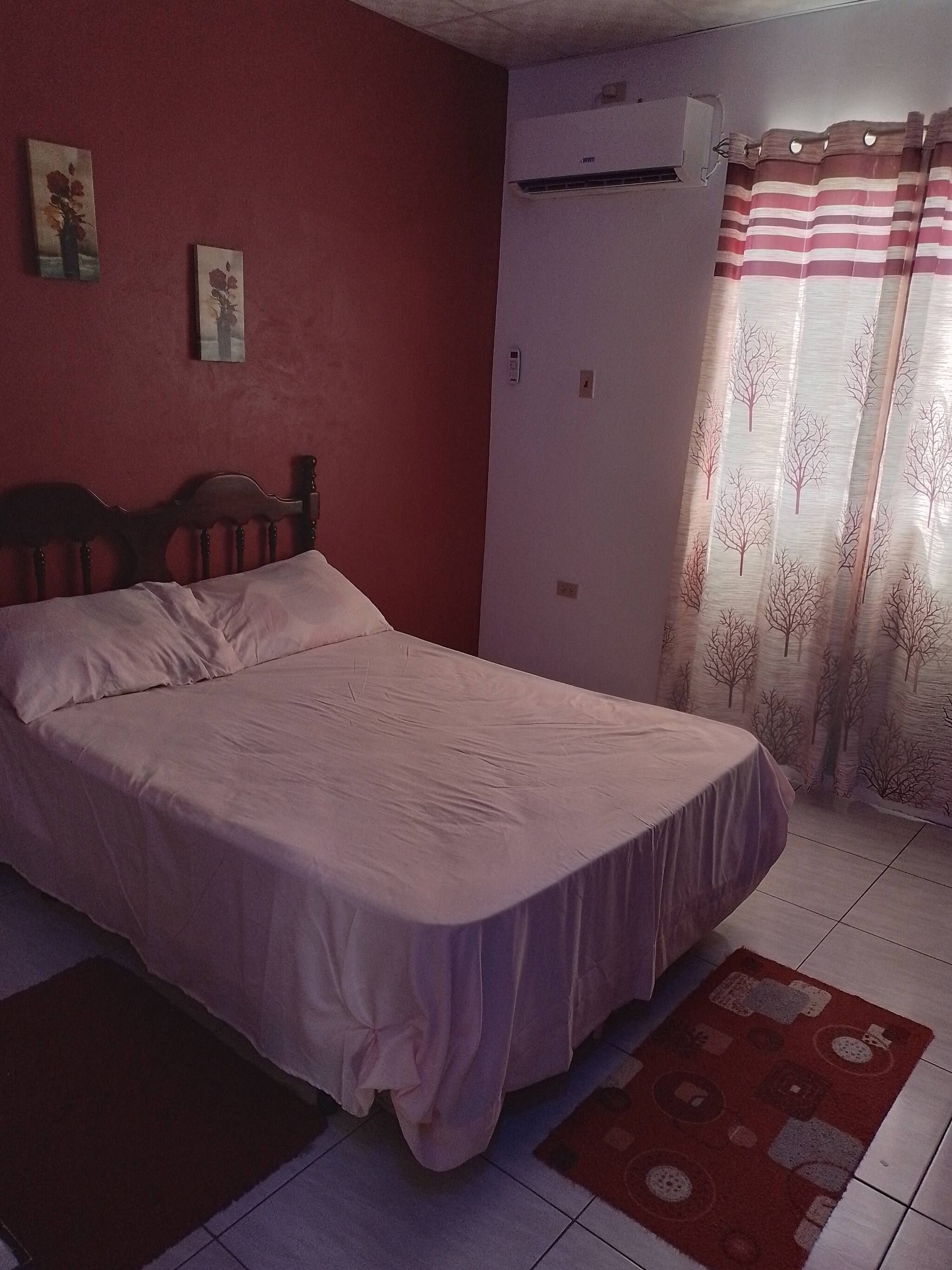 A bedroom with a bed, a wall-mounted air conditioner, and a door with a striped curtain.