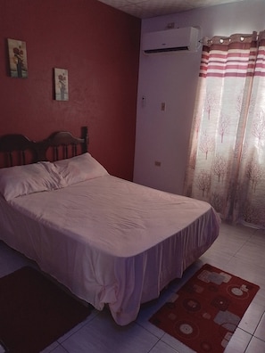 A bedroom with a bed, a wall-mounted air conditioner, and a door with a striped curtain.