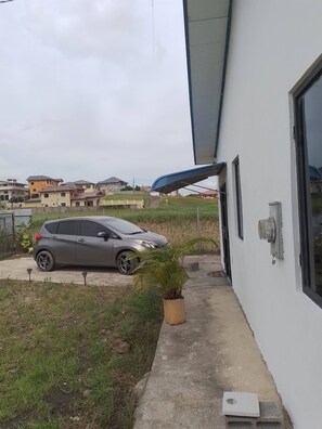 A grey car parked in a driveway, a white building with a large window, and a potted plant.