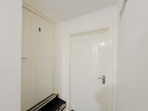 Un pasillo con dos puertas blancas, una marcada con el número 1, y un pequeño escalón que lleva a un suelo oscuro.