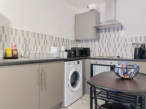 Cocina compacta con lavadora, cafetera y un bol sobre la mesa.