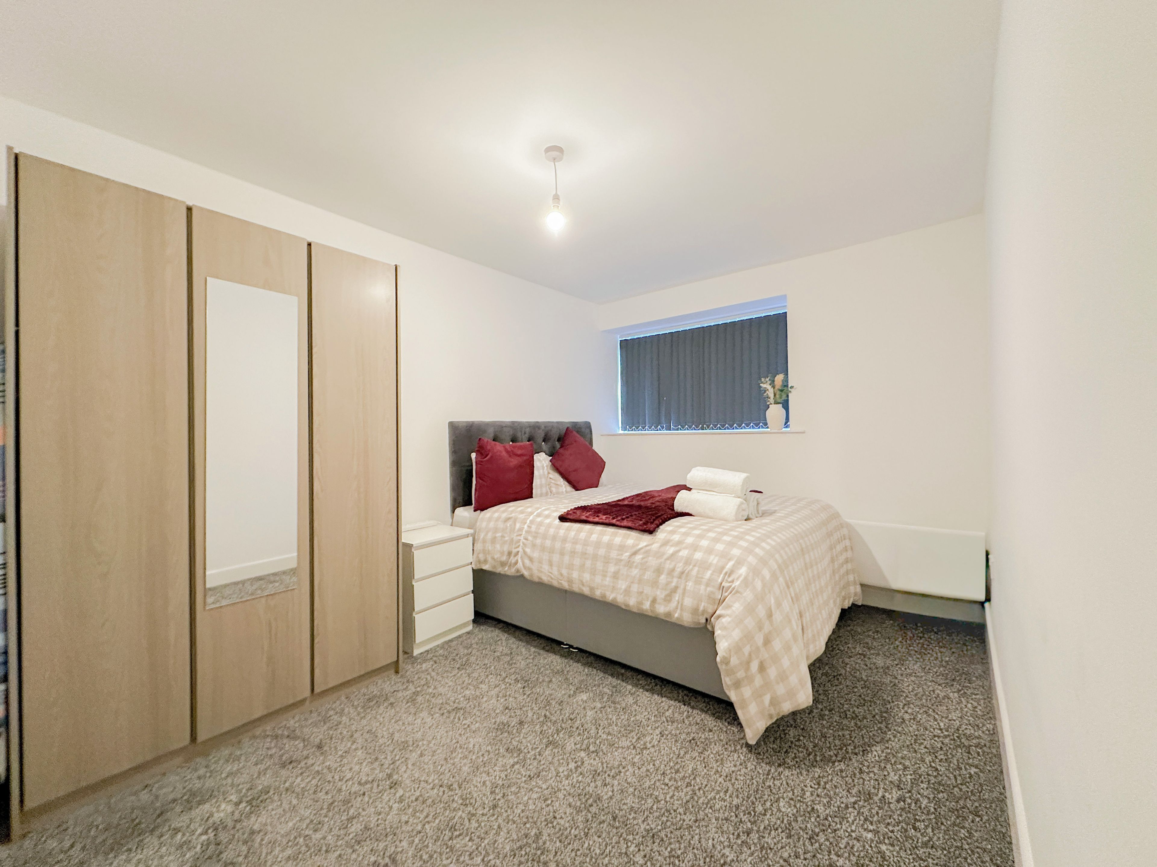 Een slaapkamer met een bed, nachtkastjes, een kledingkast en een raam met zonwering.